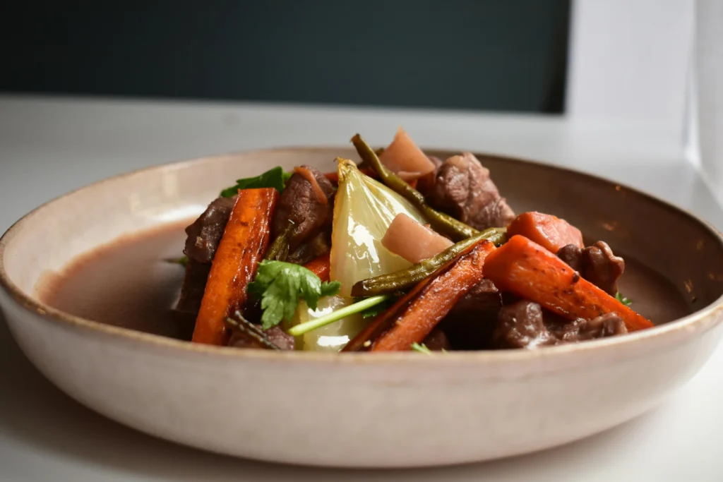 A bowl of Filipino Kaldereta, showcasing tender chunks of beef and colorful vegetables like bell peppers and carrots in a thick, reddish-brown sauce.