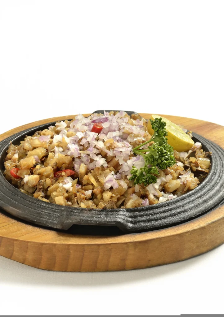 A sizzling platter of Filipino sisig, a dish made from finely chopped pork with onions and chili, garnished with a raw egg and served on a cast iron plate.