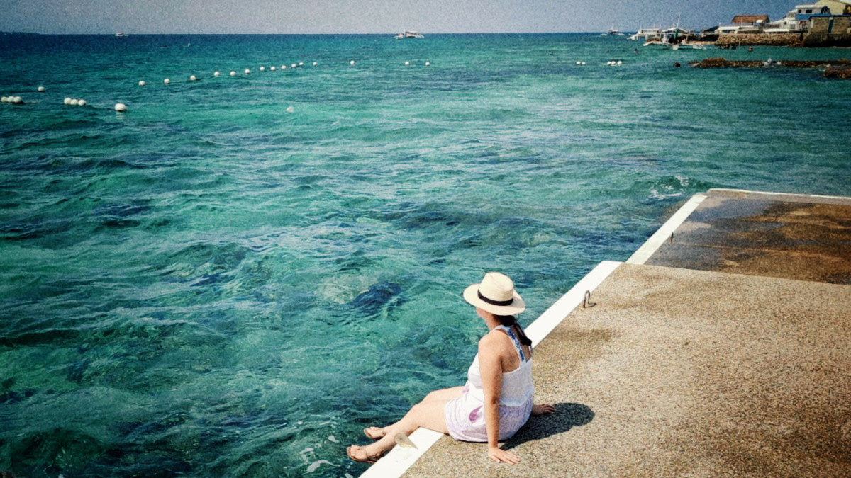 Photo of a woman in a sun hat looking out at the turquoise ocean in Cebu, Philippines.