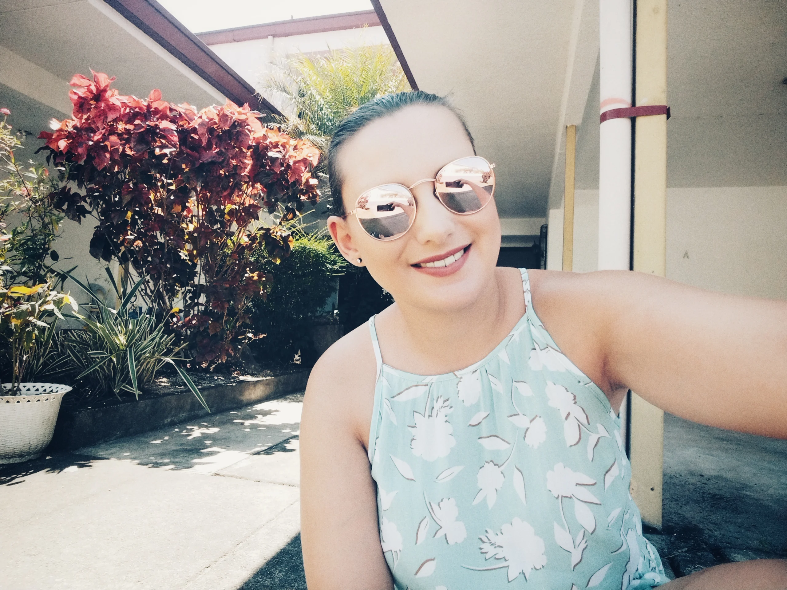 Smiling photo of a woman in sunglasses wearing a floral top, relaxing outdoors in the Philippines.