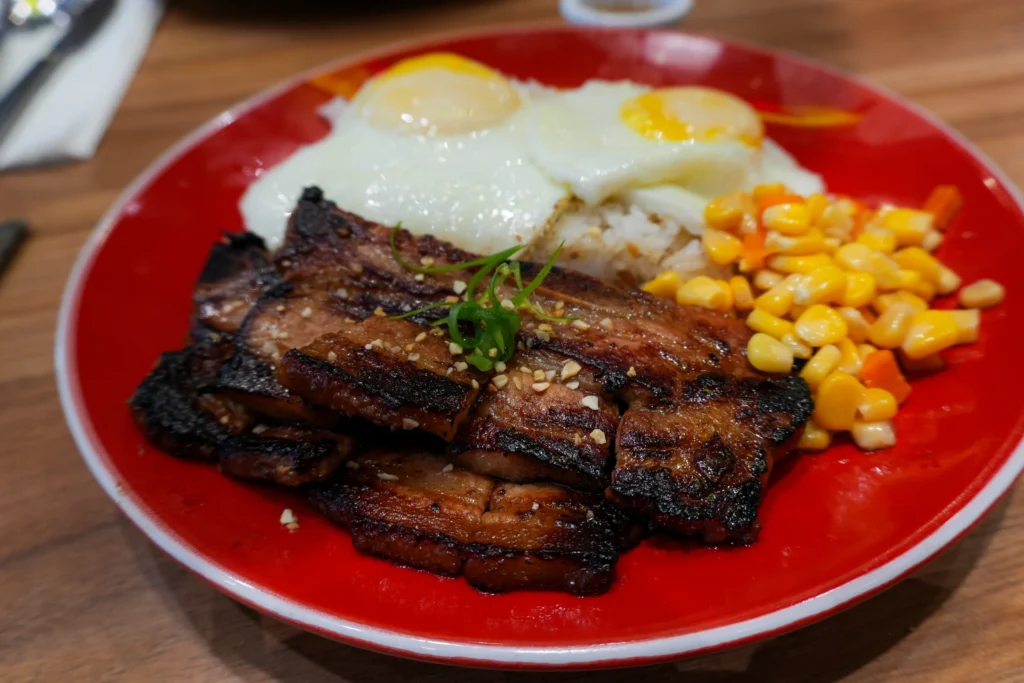 A serving of Filipino liempo, showing slices of grilled pork belly with a golden-brown, crispy skin and a juicy interior.