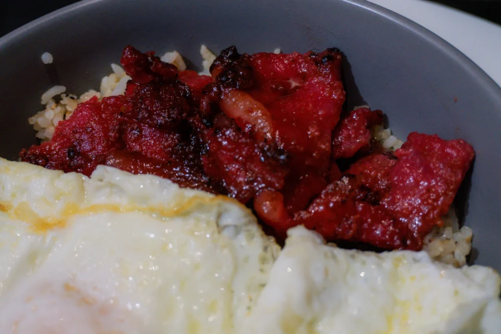 A close-up shot of a plate of Filipino pork tocino, showcasing the vibrant red-orange color of the marinated pork slices.