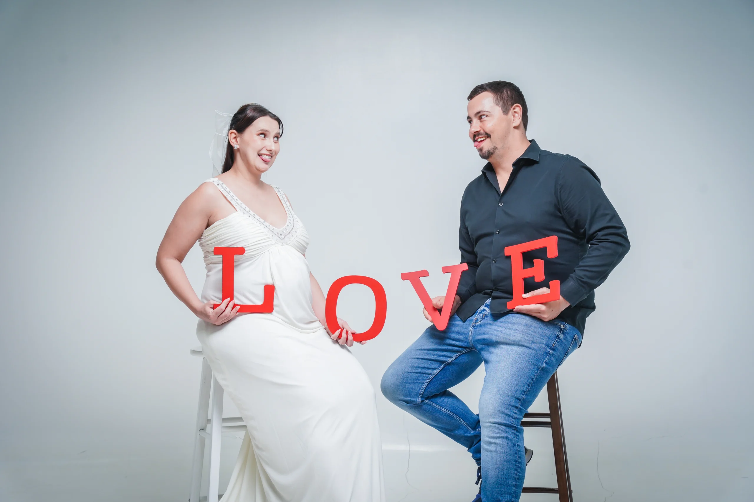 Smiling pregnant woman and her husband holding red "LOVE" letters for a maternity photoshoot.