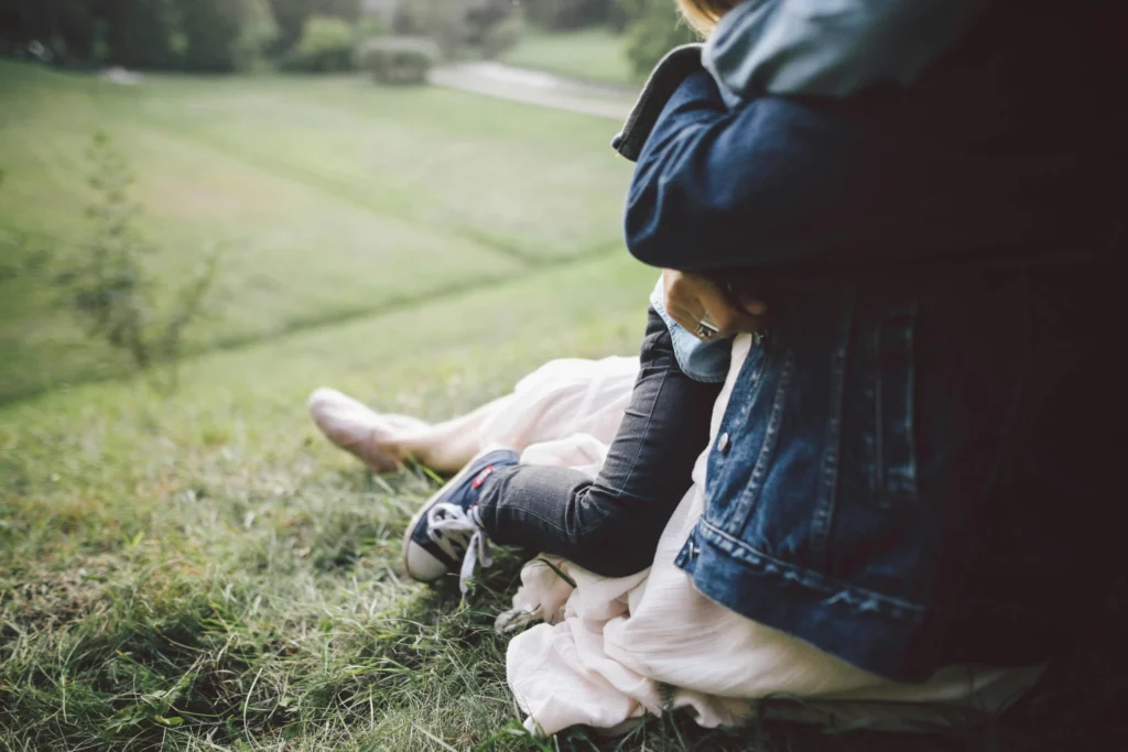 Mother sitting on the grass holding her child closely, sharing a quiet and comforting moment outdoors.